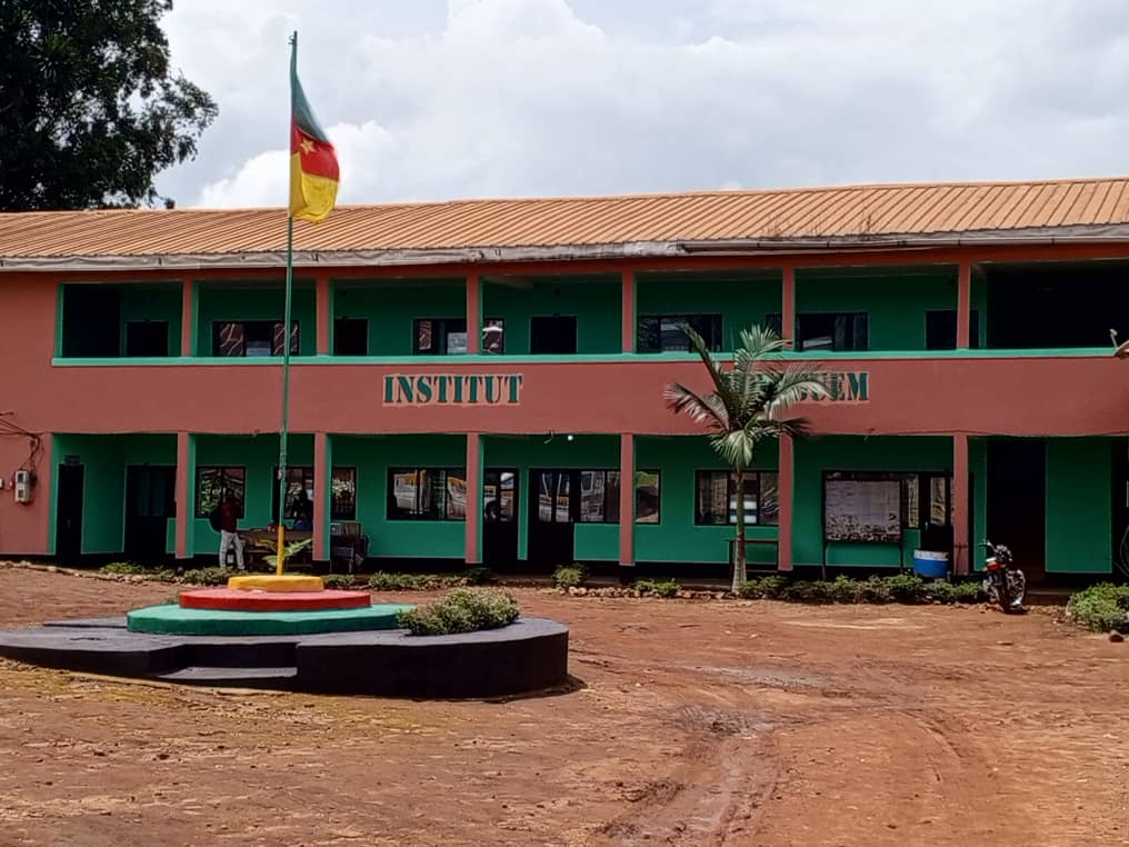 Façade du bâtiment principal et drapeau camerounais hissé au centre de la cour.